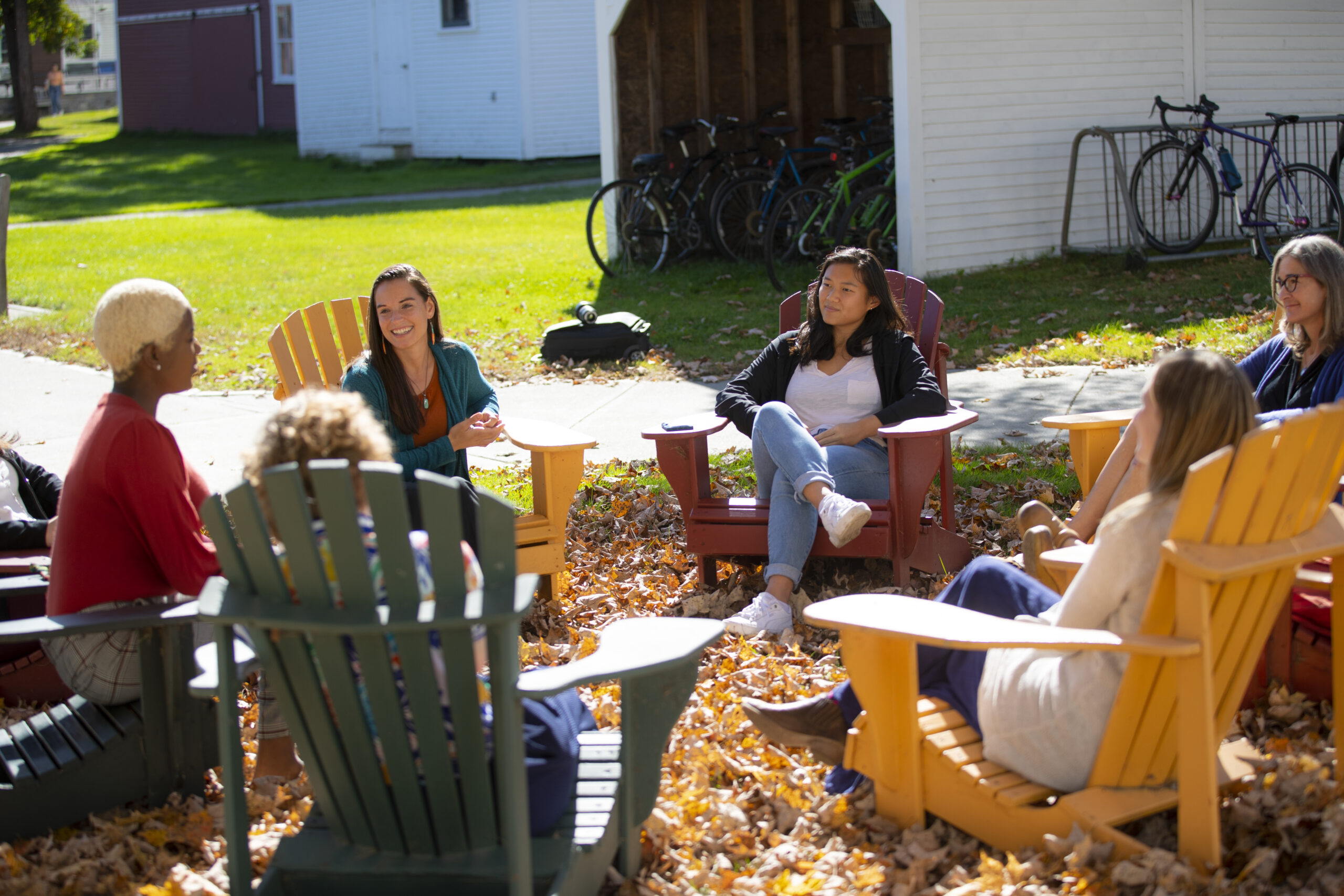 Decorative: a diverse group of six smiling people sitting outside in a circle of multicolored wooden lawn chairs